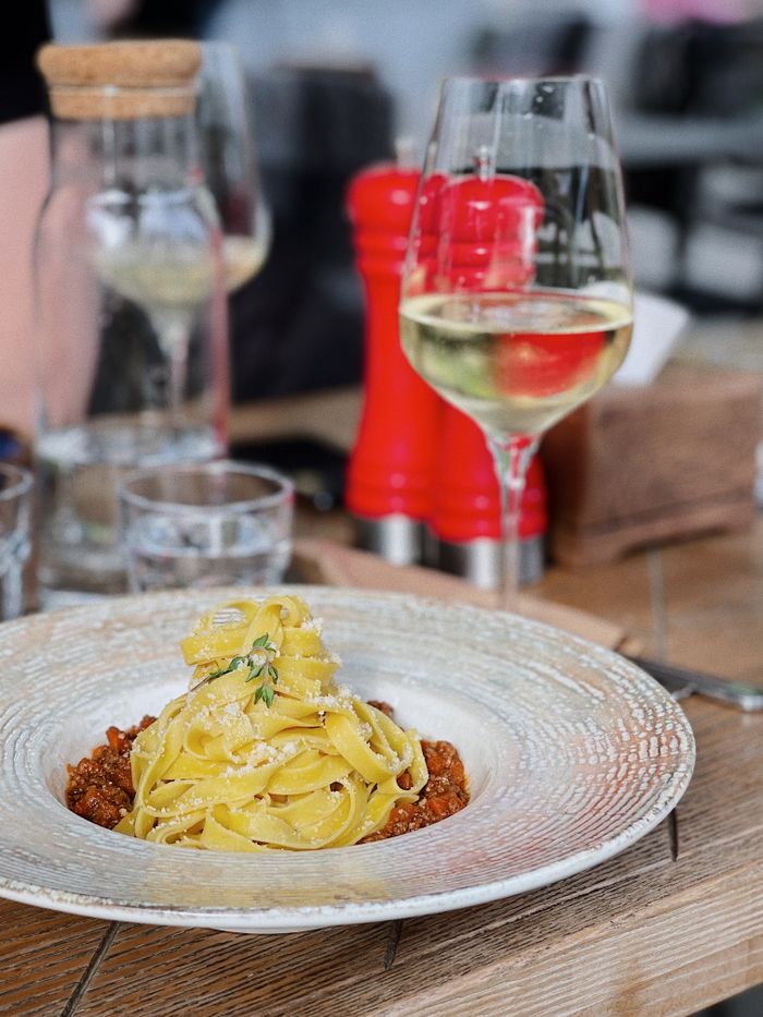 A plate of tagliatelle pasta served with a glass of white wine in a restaurant setting.