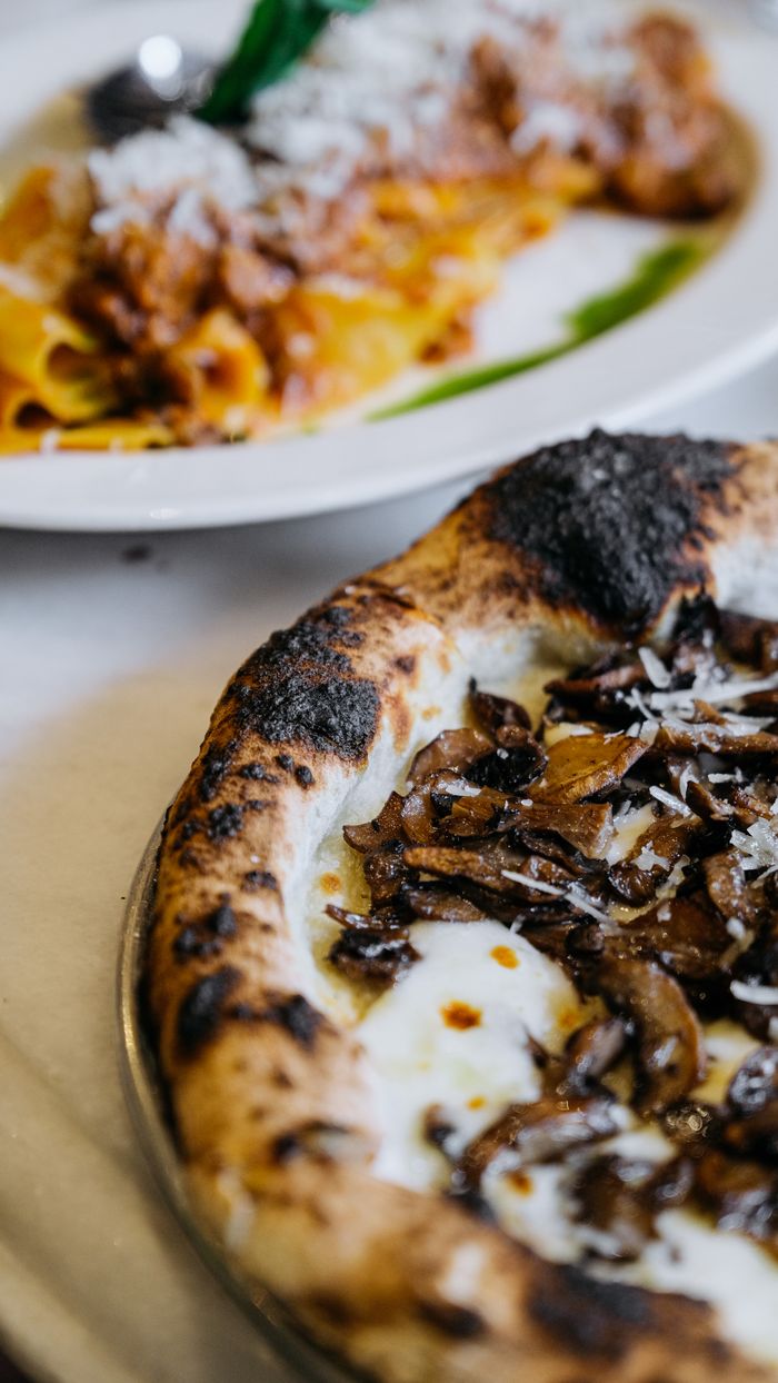 Close-up of a burnt crust pizza topped with mushrooms alongside a delicious pasta dish.