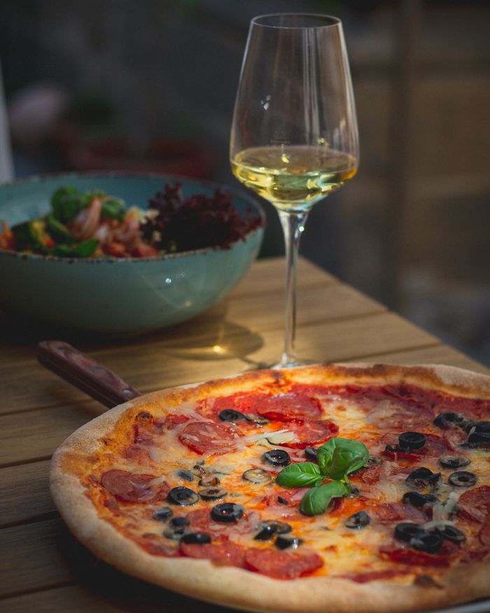 Tasty pepperoni pizza served with white wine outdoor, perfect for dining delight.