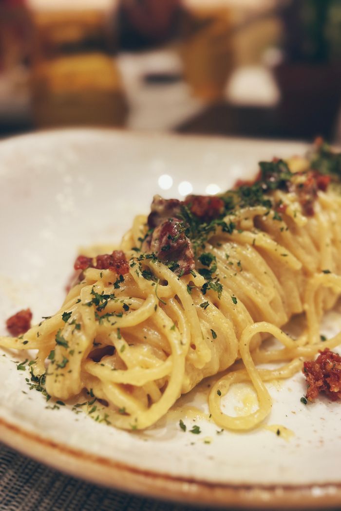 Close-up of creamy spaghetti carbonara with herbs and bacon garnish.