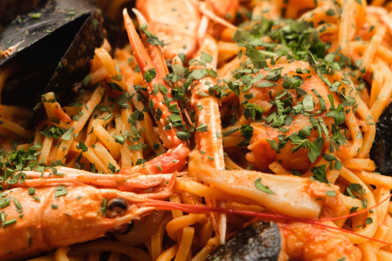 Closeup of dish from pasta and shrimps under green herbs with sauce in restaurant